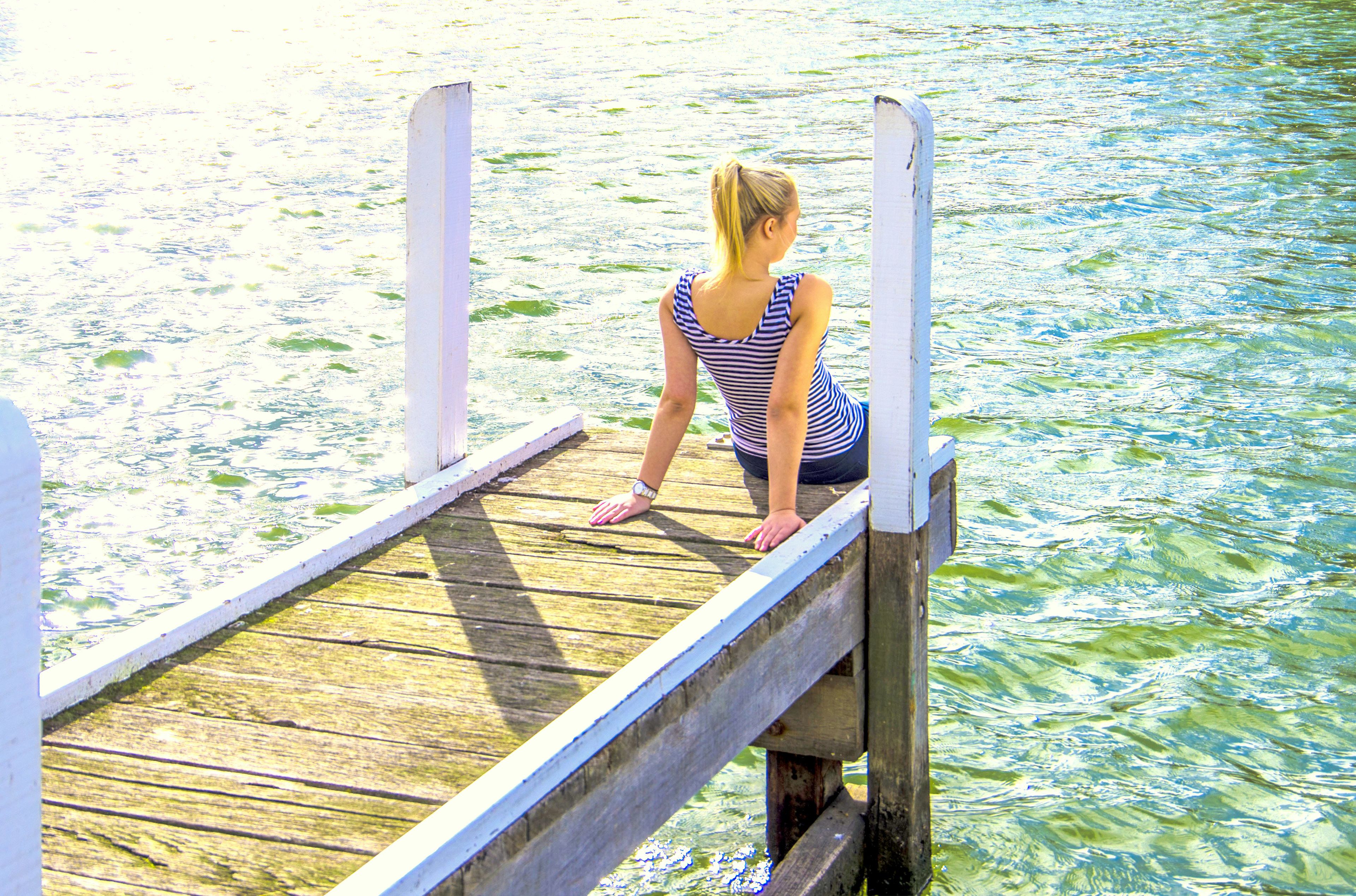 Iemand zit op een houten steiger die over het water uitsteekt.