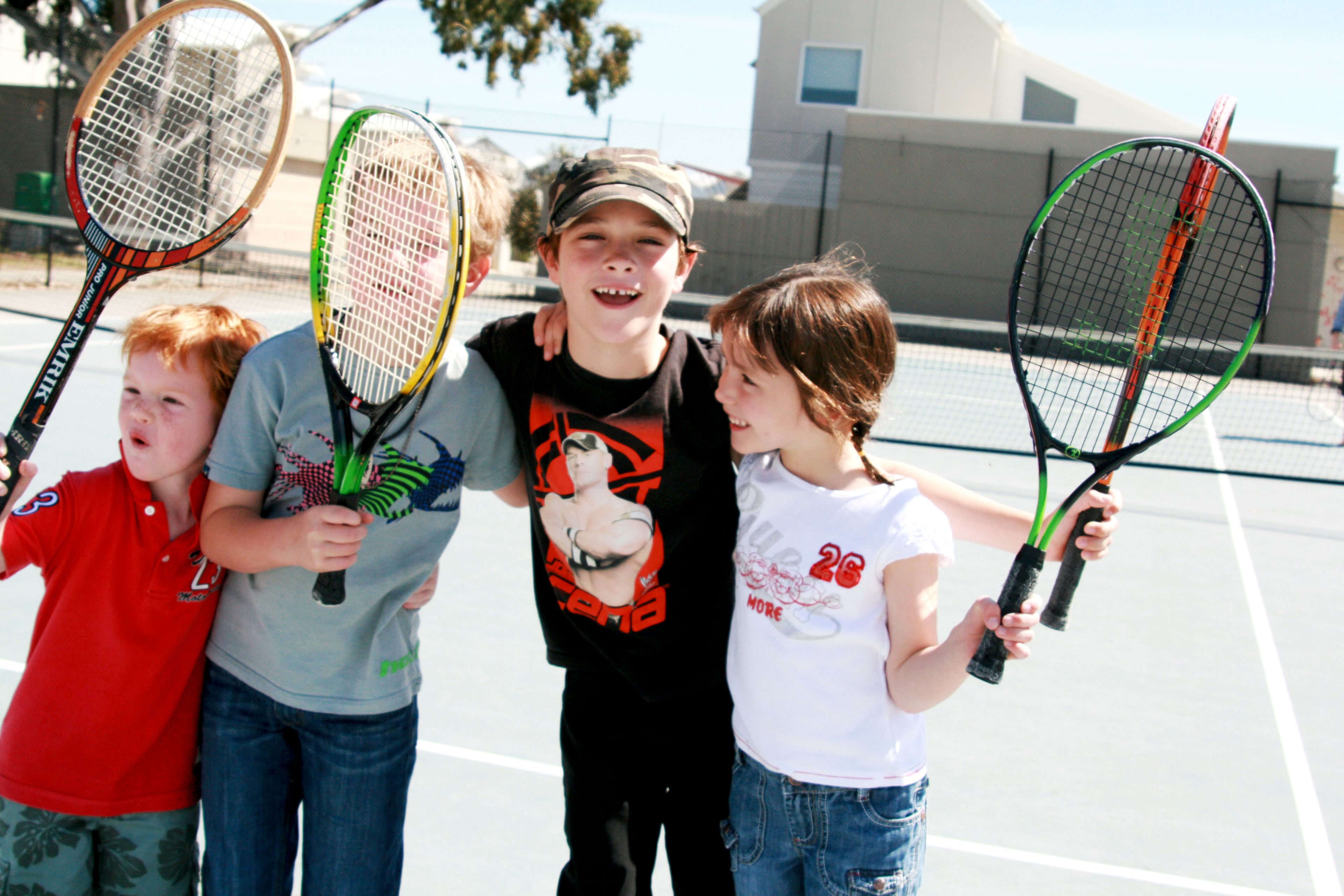 A group of children holding tennis rackets on a tennis court.