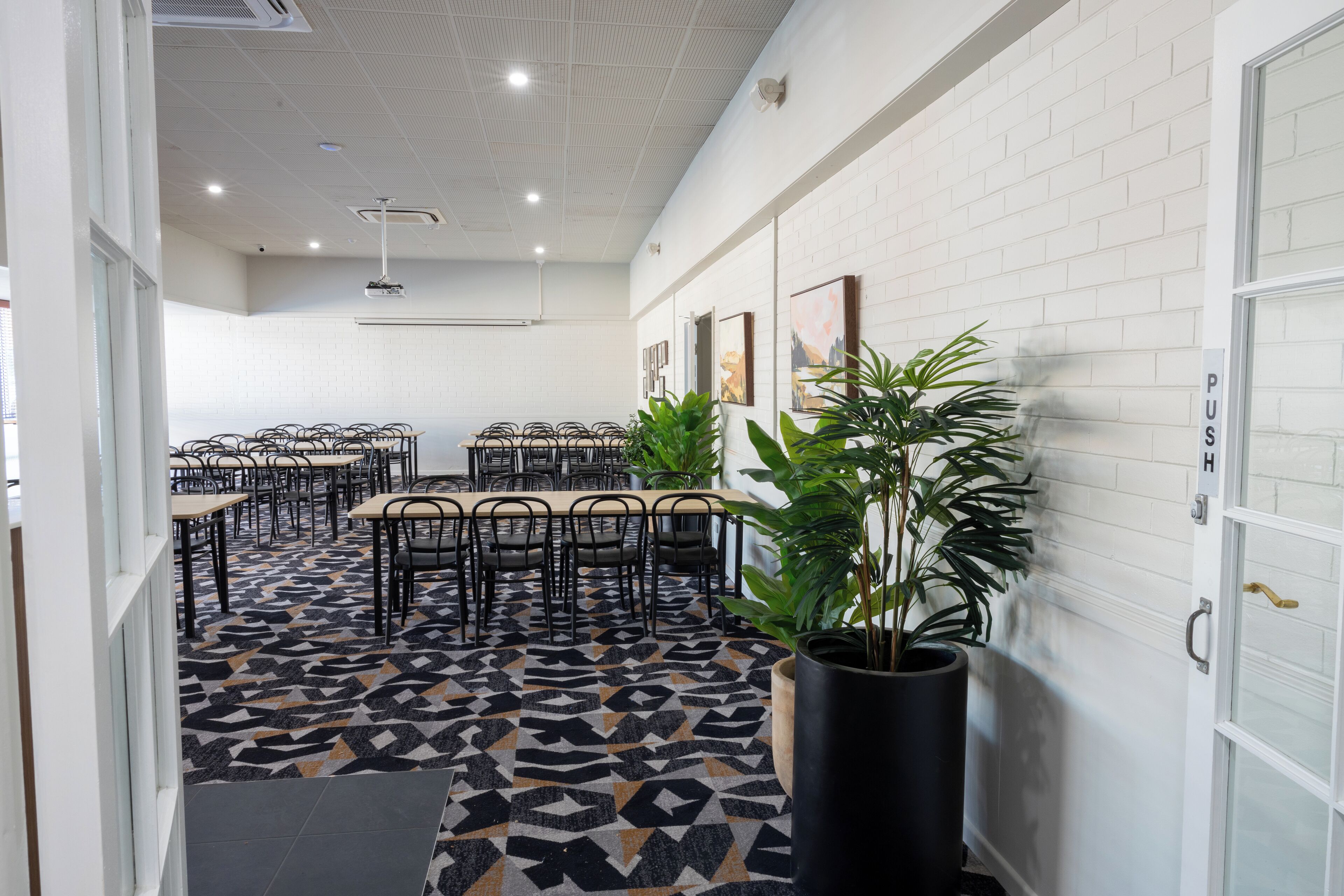A modern meeting room with a geometric patterned floor, white brick walls, and several tables and chairs.