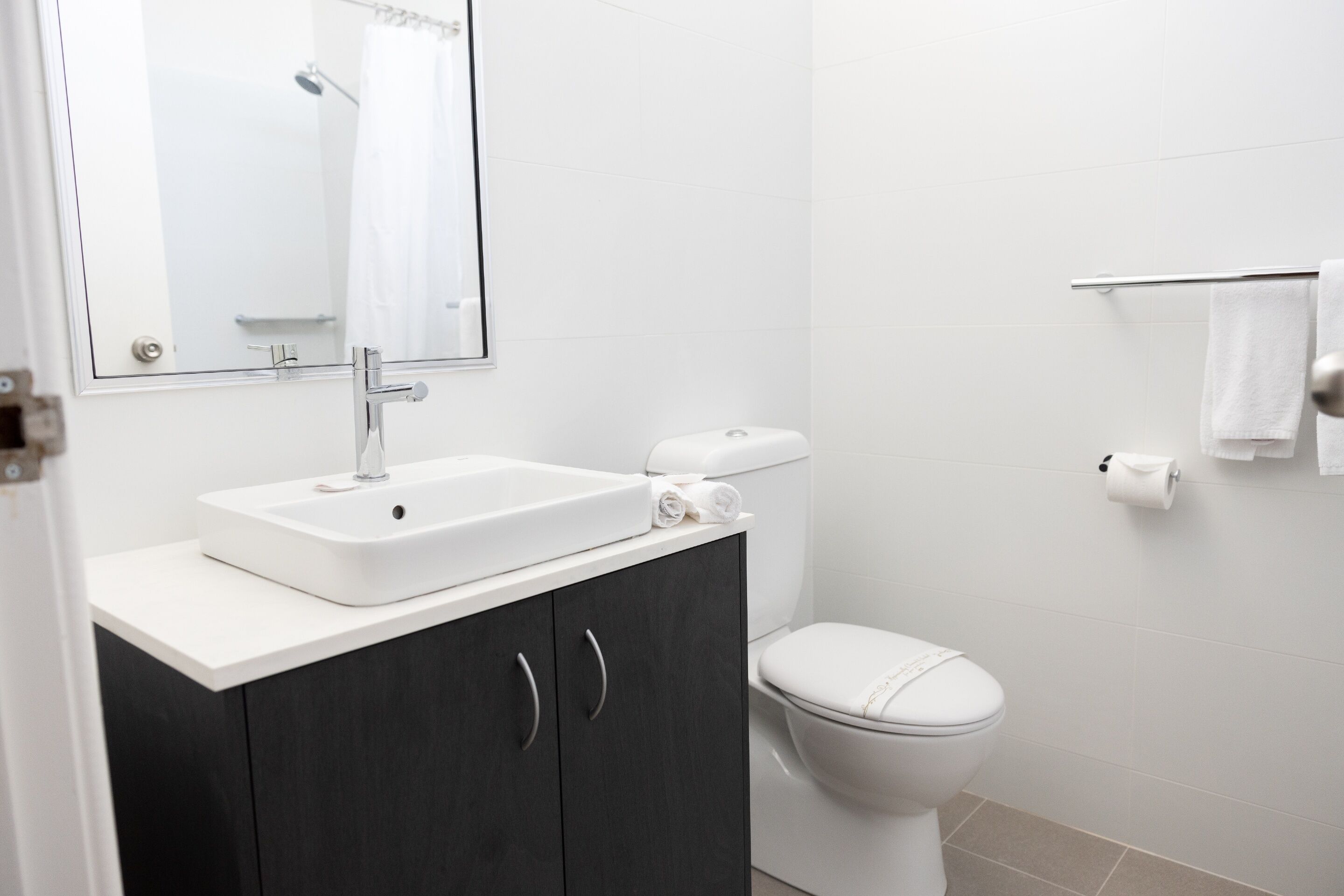 Een moderne badkamer met een wit wastafel, donkere kastjes, een toilet en een handdoekhouder.