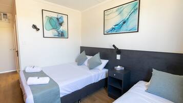 A hotel room with two beds, a dark headboard, a bedside table with a lamp, and artwork on the walls.