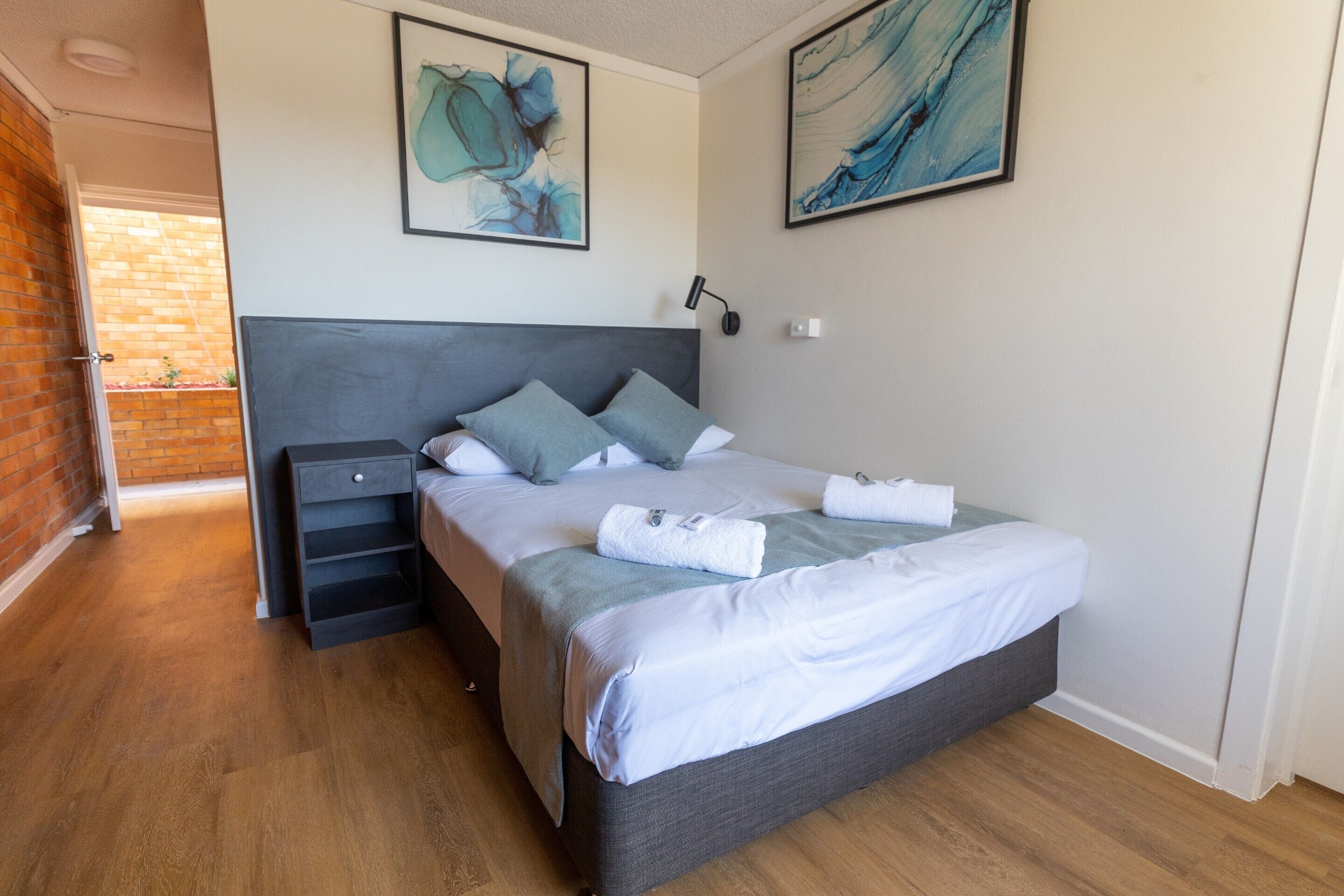 Een moderne slaapkamer met een grijs hoofdeinde, een houten vloer en twee schilderijen aan de wand.