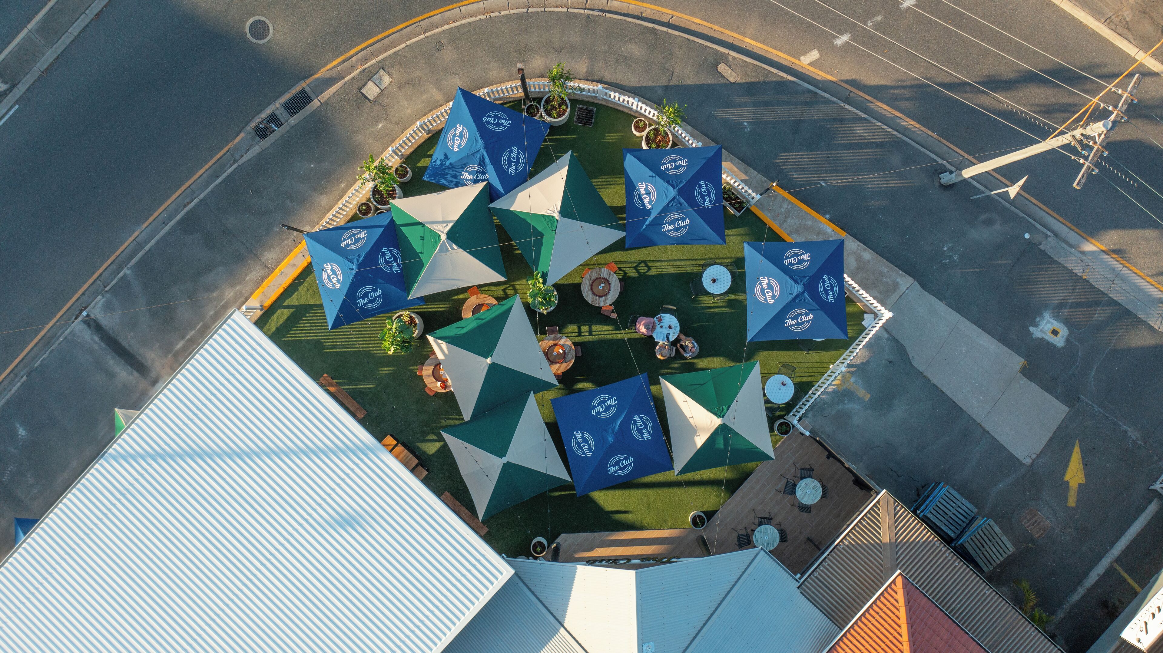 An aerial view of a rooftop terrace with multiple tables and umbrellas, surrounded by buildings.