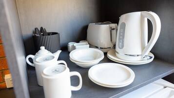 Uma bancada de cozinha com utensílios brancos, incluindo chaleira, bule, xícaras e pratos.