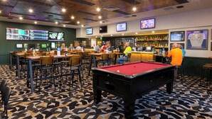 A pool table in a bar area with multiple screens displaying sports content. - The Club Hotel (Gladstone)