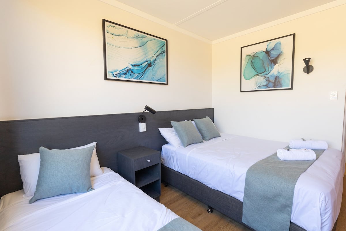 A hotel room with two beds, a nightstand, and artwork on the walls.