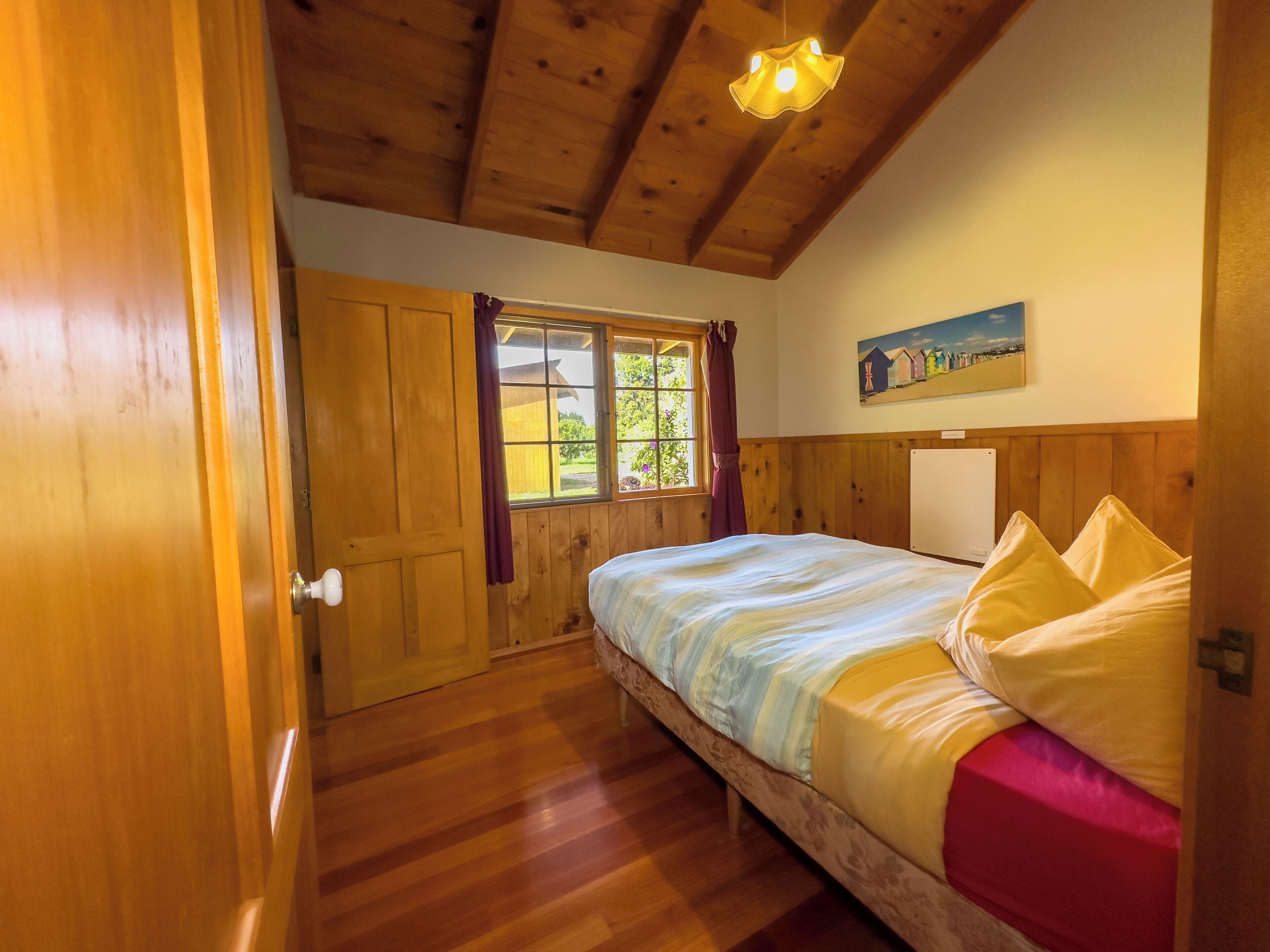 A wooden-paneled bedroom with a bed, a window with curtains, and a painting on the wall.