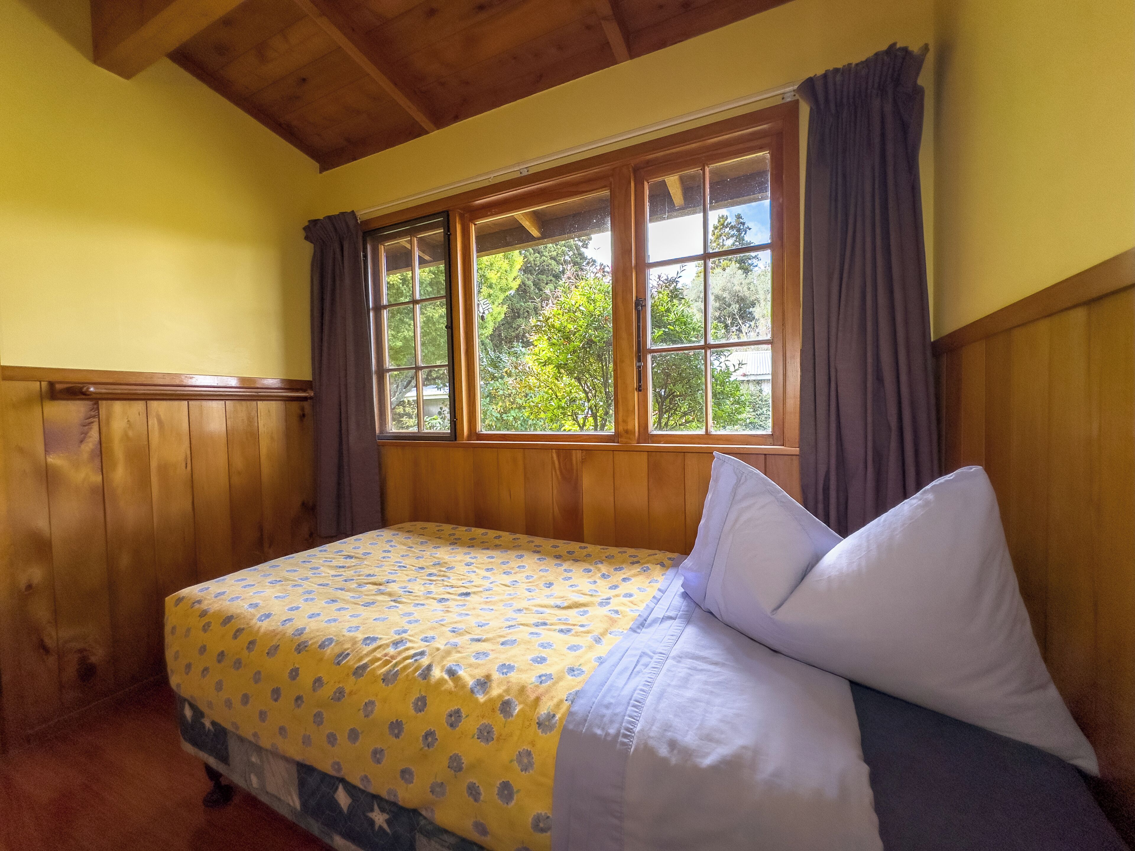 Um quarto com cabeceira de madeira, cama com colcha floral e janela com cortinas.
