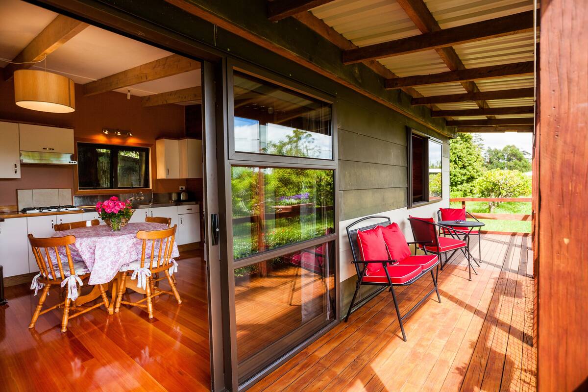 A modern kitchen with wooden cabinets, a dining table with chairs, and a large window overlooking a garden.