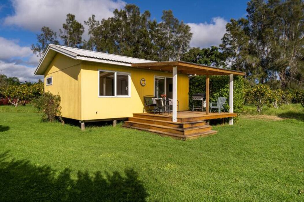 Una casa amarilla de un piso con porche cubierto y una pequeña terraza.
