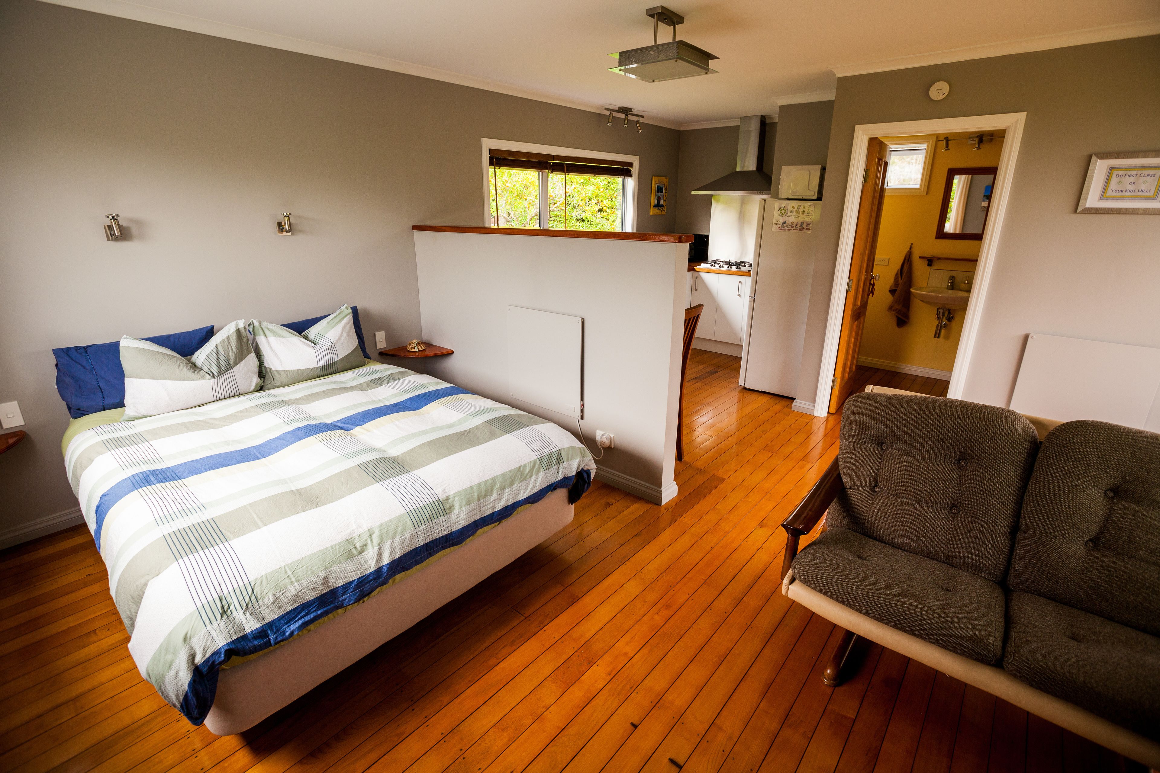 Ein Schlafzimmer mit Bett, Stuhl, Fenster und einer kleinen Küche.