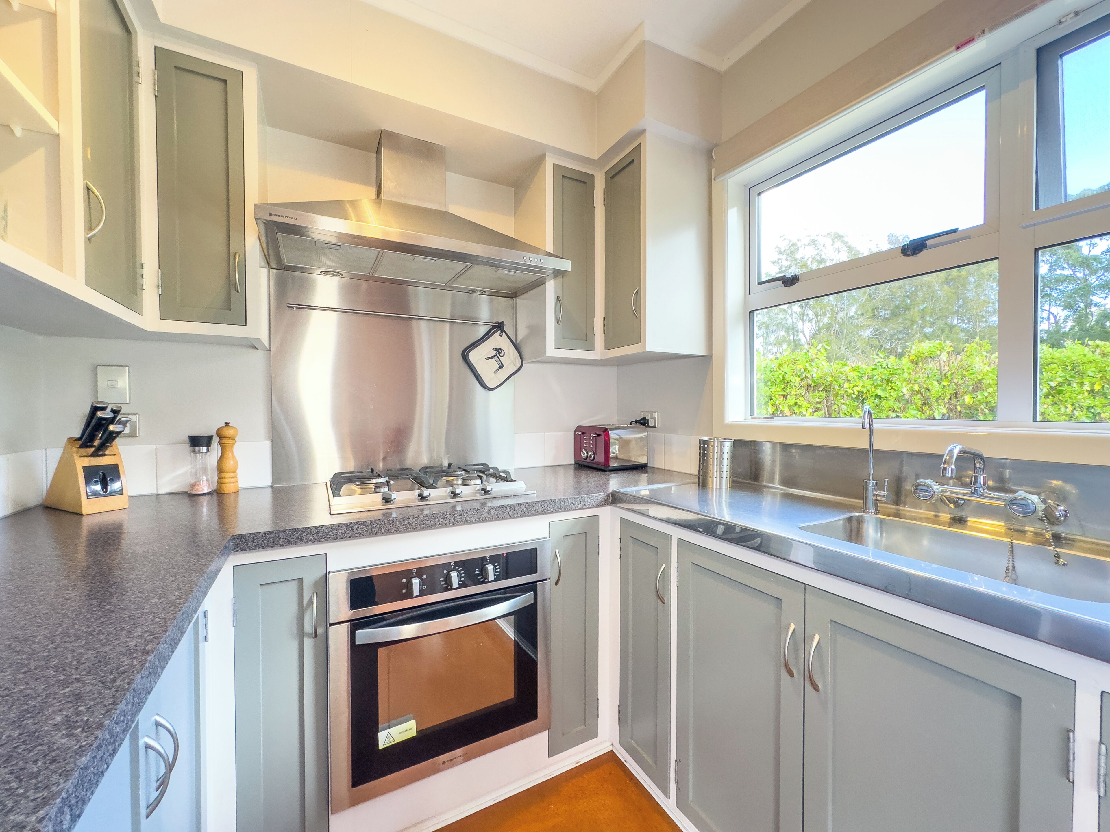 A modern kitchen with stainless steel appliances, a built-in oven, and a window providing a view of greenery outside.