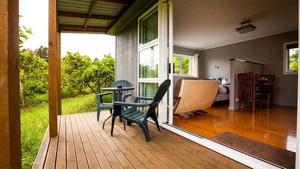 A covered outdoor area with a wooden deck, a table, and chairs. - Relax a Lodge (Kerikeri)