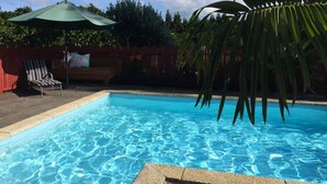 A swimming pool with clear blue water, surrounded by a red fence, a wooden bench, and a green umbrella. - Relax a Lodge (Kerikeri)