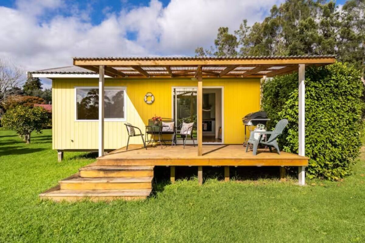 A yellow single-story house with a wooden deck, a covered patio, and a barbecue area.