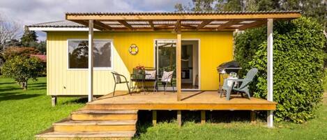 A yellow house with a wooden deck, a covered patio, and a barbecue area.