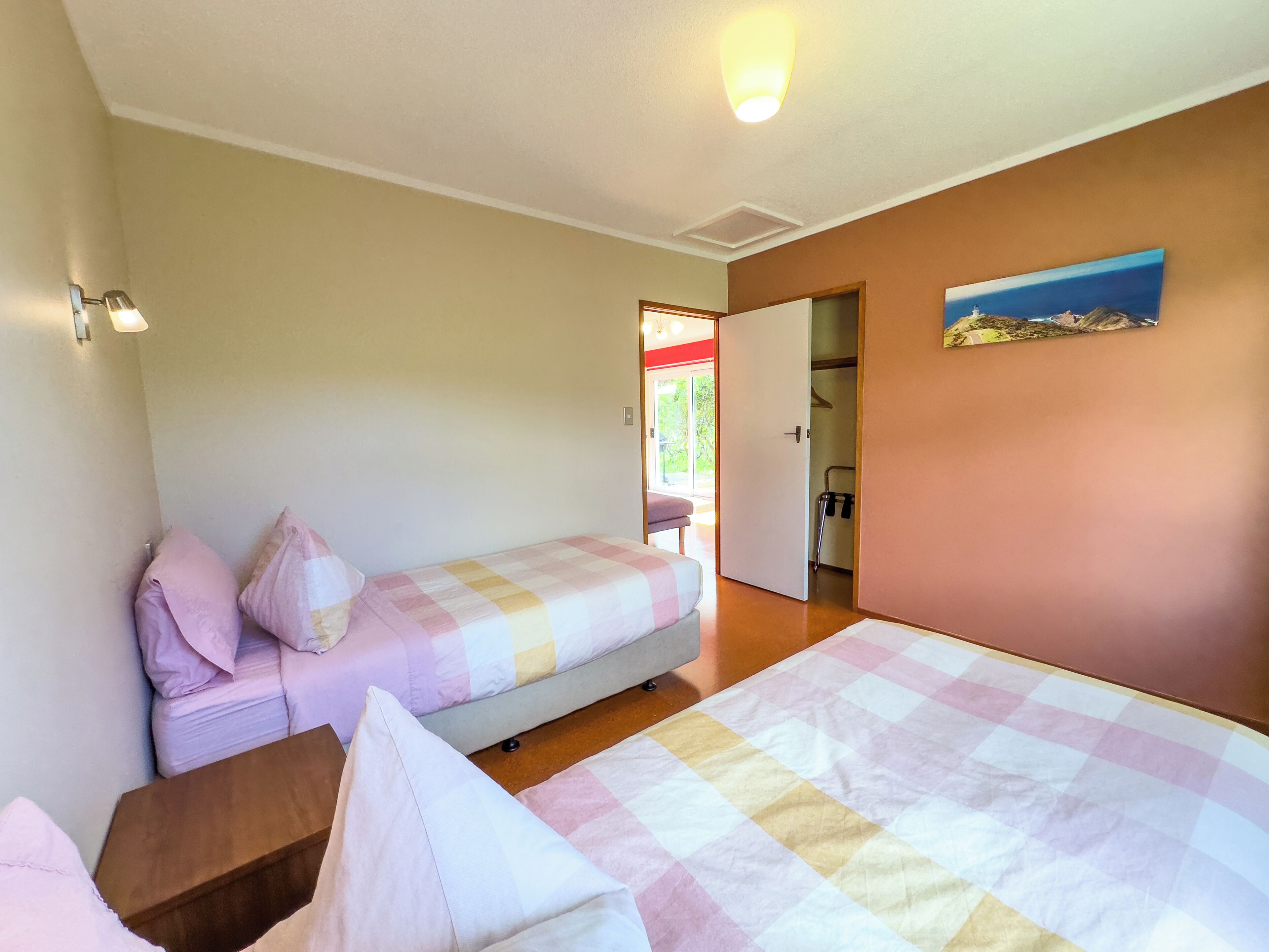 Une chambre avec deux lits, une table de chevet en bois, une porte donnant sur une salle de bain et un tableau accroché au mur.