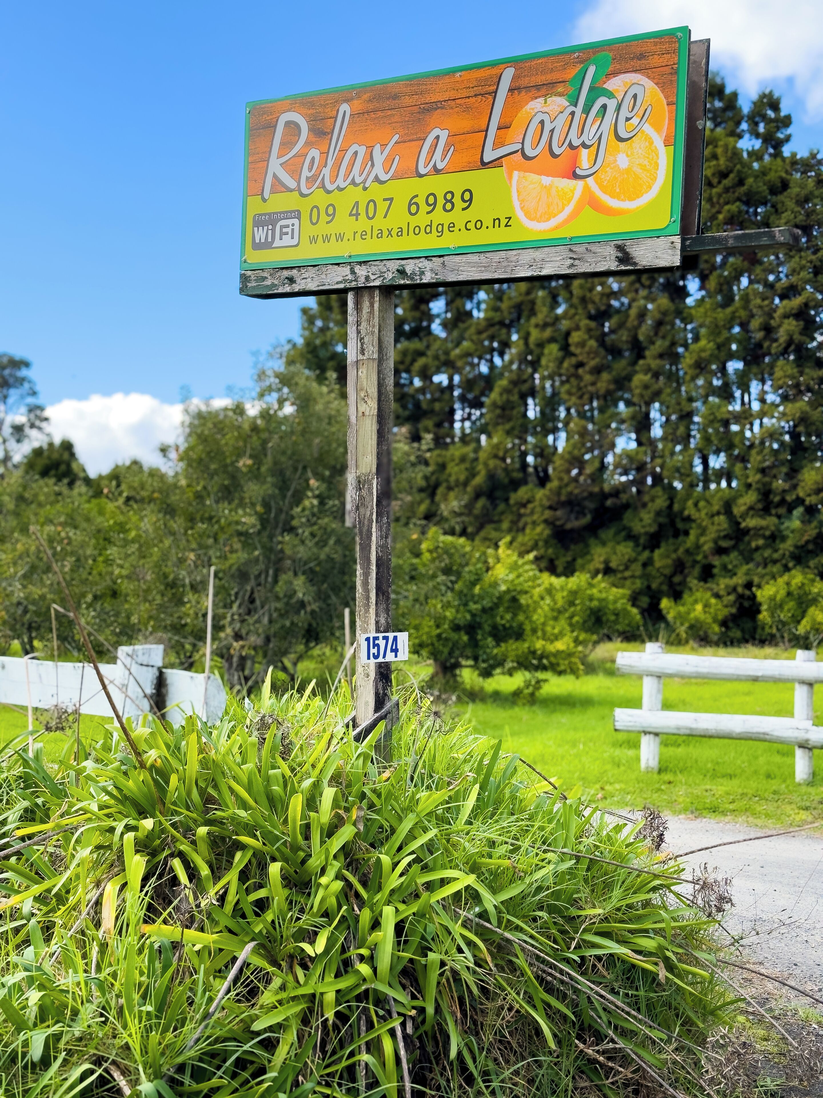 A wooden signboard for 'Relax a Lodge' with contact information and a website URL.