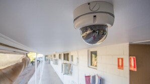 Un couloir équipé d’une caméra de surveillance fixée au plafond, d’une fenêtre offrant une vue dégagée et d’un détecteur d’incendie mural.