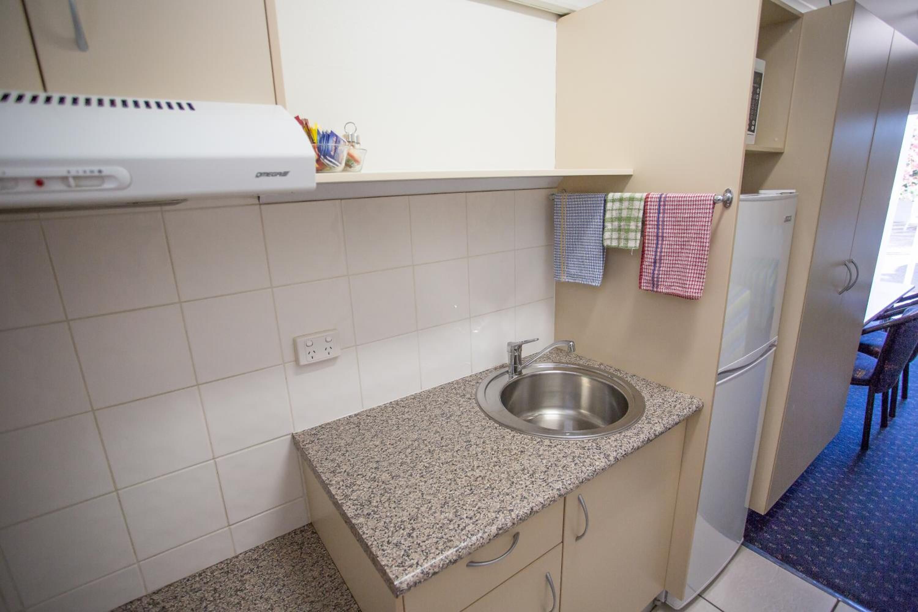 Cocina compacta con encimera de granito, pileta de acero inoxidable y refrigerador blanco.