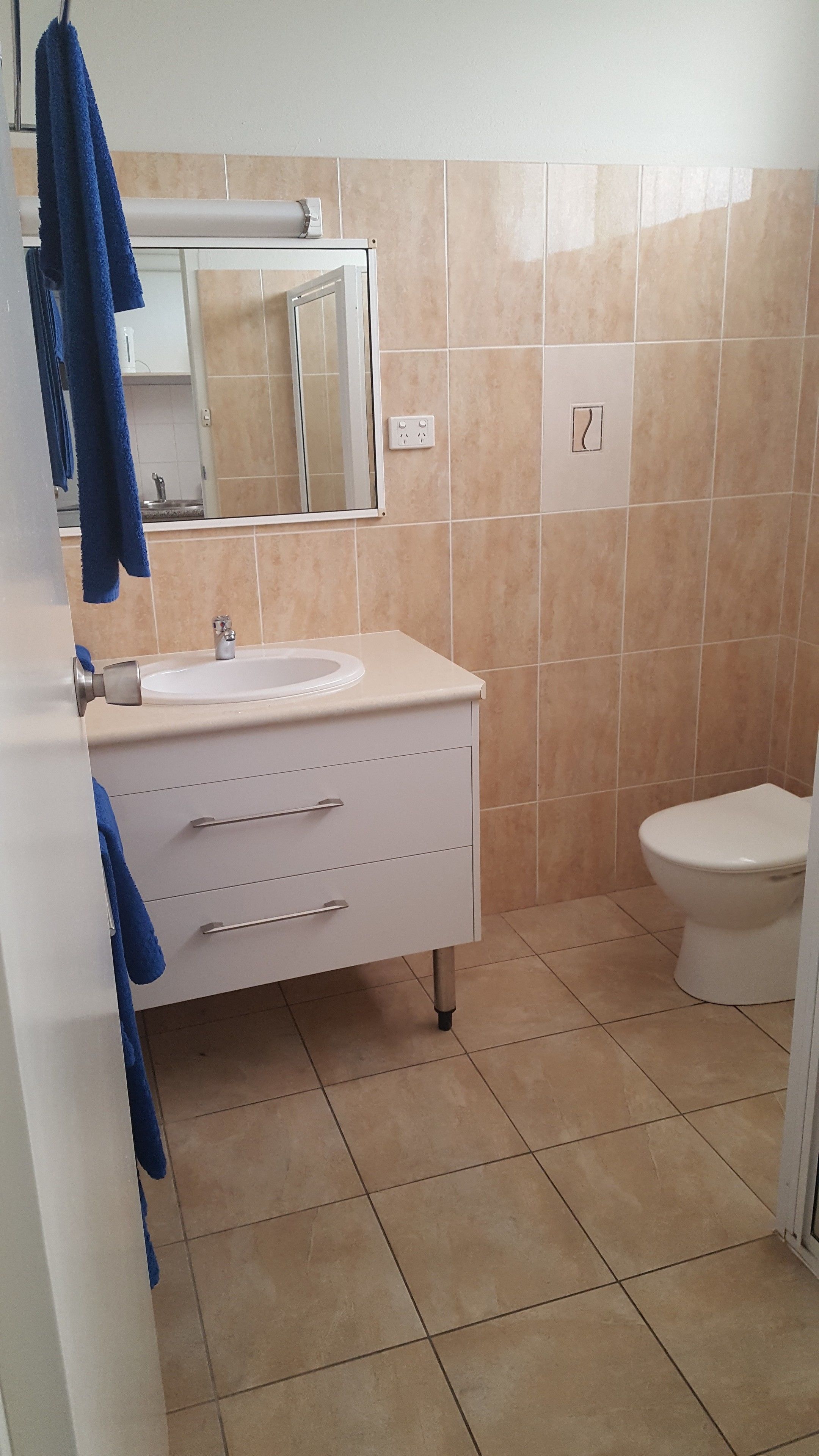 Ein Badezimmer mit Waschbecken, Spiegel und Toilette. Die Wände und der Boden sind mit beige gefliest.