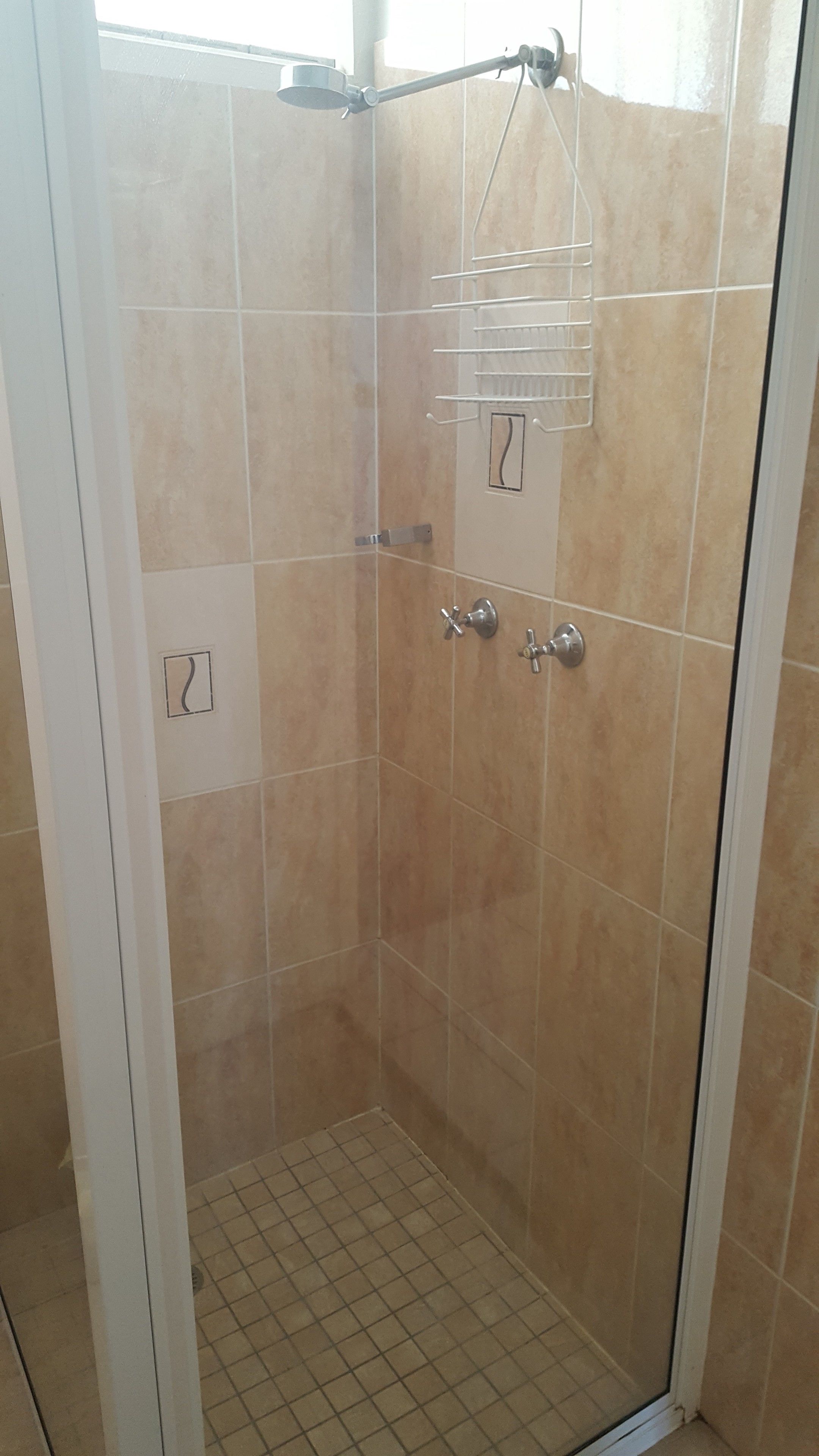 A glass-enclosed shower area with beige tiles, a handheld showerhead, and a wall-mounted towel rack.