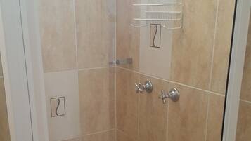 A glass-enclosed shower area with beige tiles, a handheld showerhead, and a wall-mounted towel rack.