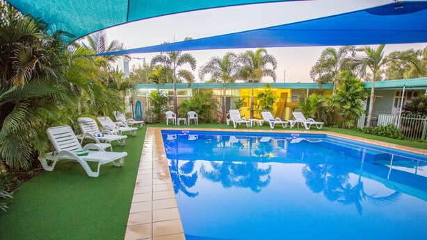Une piscine entourée de chaises longues blanches et d’un espace abrité sous une tonnelle bleue.