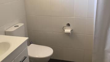 Un baño con inodoro blanco, lavamanos blanco con espejo y suelo de baldosas negras.