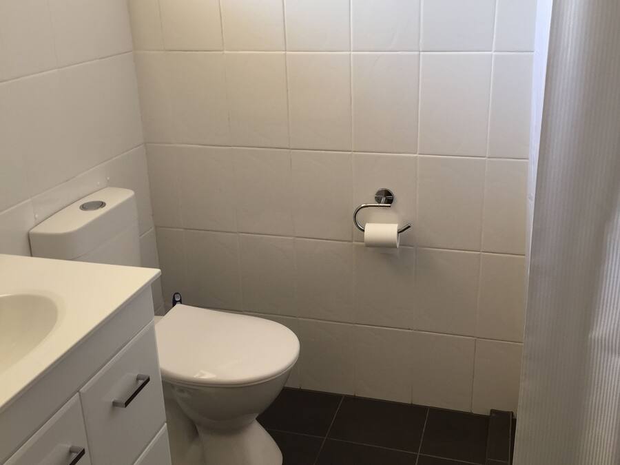 Un baño con inodoro blanco, lavamanos blanco con espejo y suelo de baldosas negras.