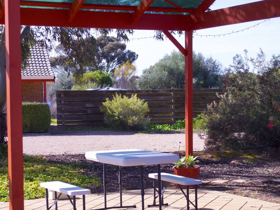 Una zona patio coperta con un tavolo e due sedie, circondata da un recinto di legno e diverse piante.