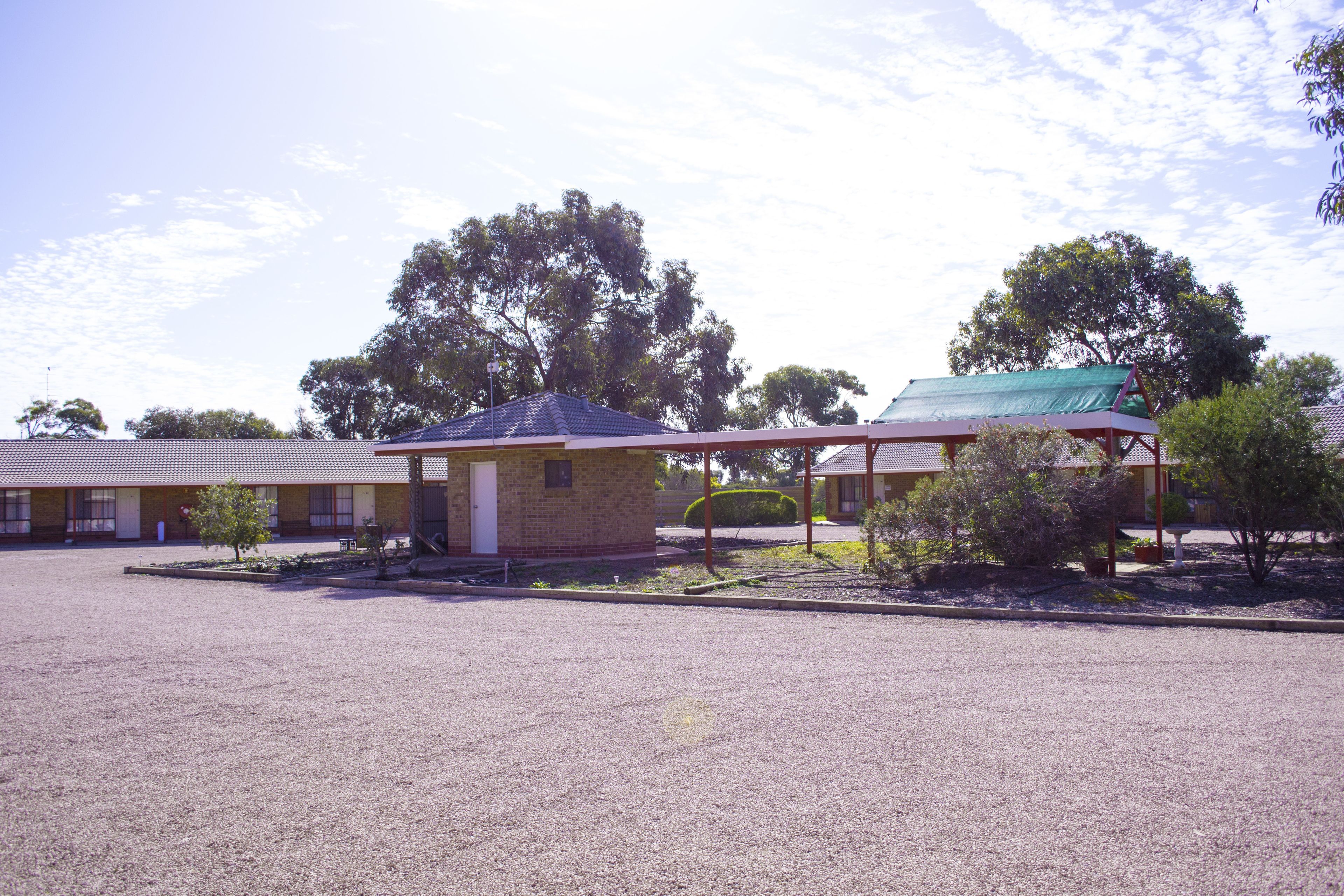 A motel with a gravel parking lot, a small building with a blue roof, and trees in the background.