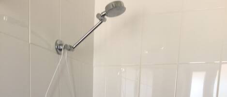 Une salle de bain carrelée de carreaux blancs, une douche avec un pommeau de douche amovible et une étagère en verre.