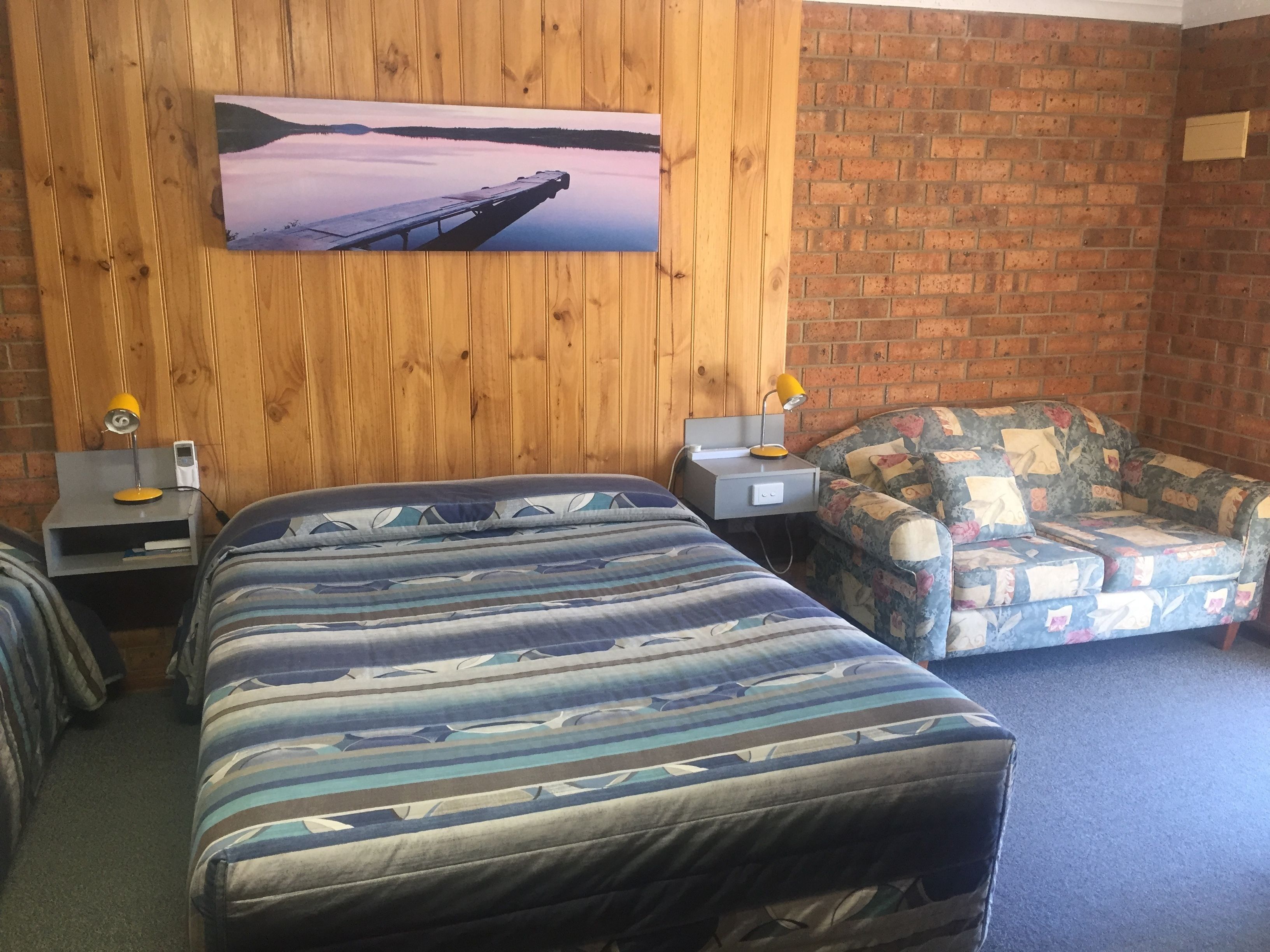 Une pièce comprenant un lit, une chaise, un bureau avec une lampe et un tableau au mur.