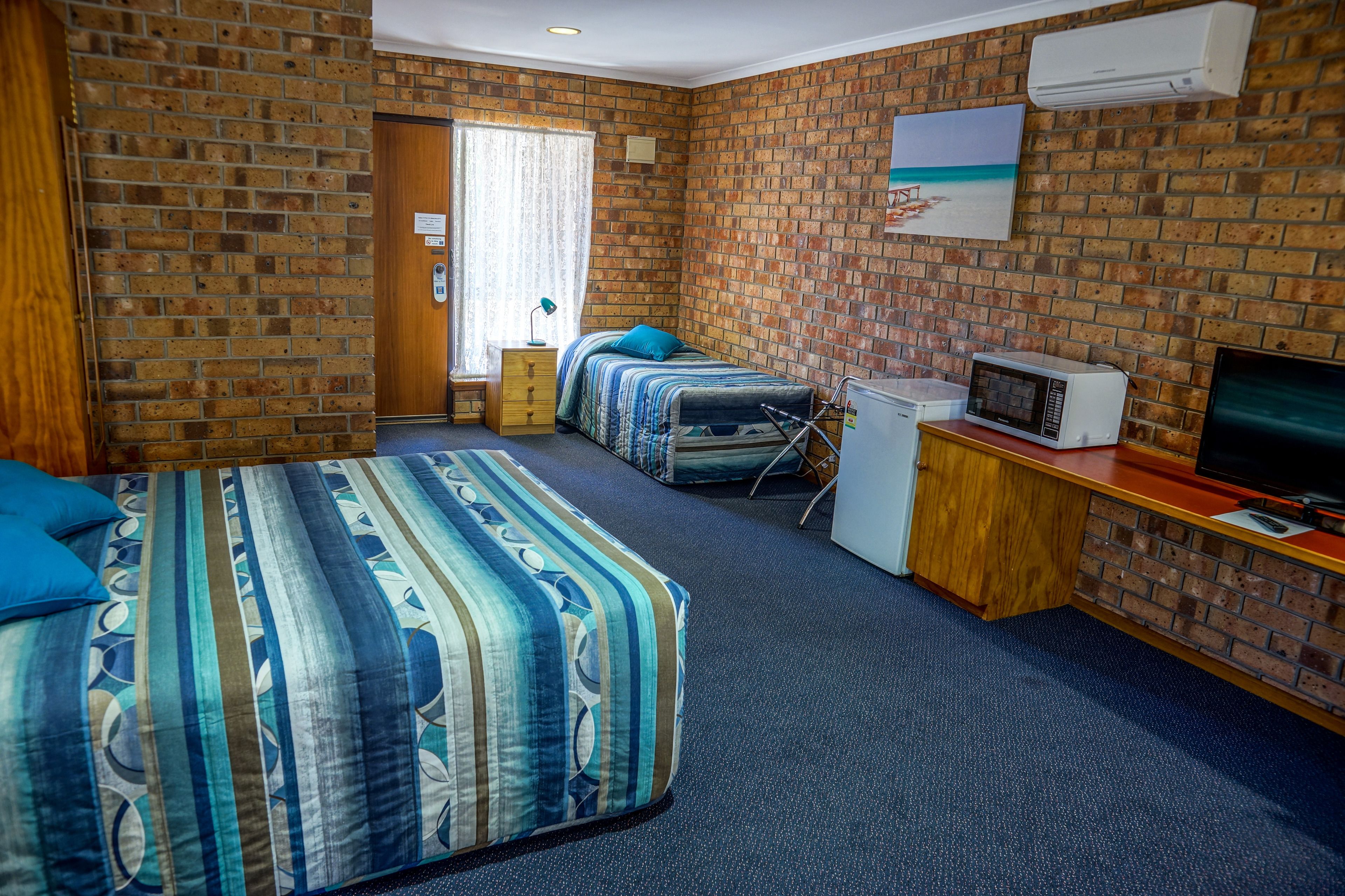 A hotel room with two beds, a TV, a microwave, and a brick wall.