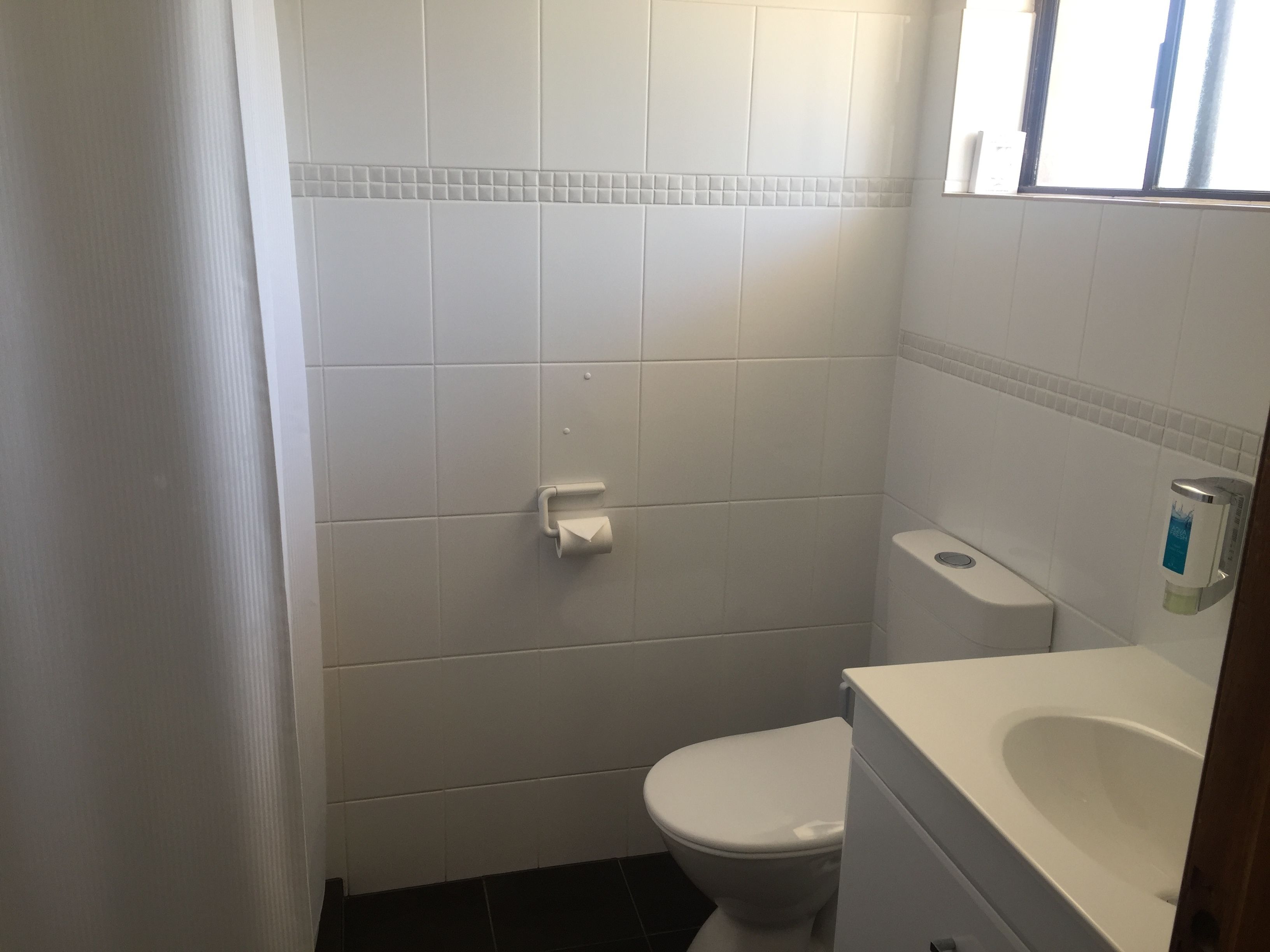 A small, clean bathroom with white tiles, a toilet, and a sink.
