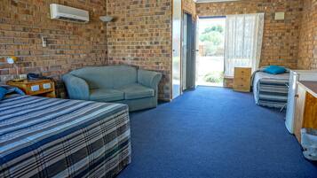 A room with a brick wall, a sofa, a bed, a desk, and a window with curtains.