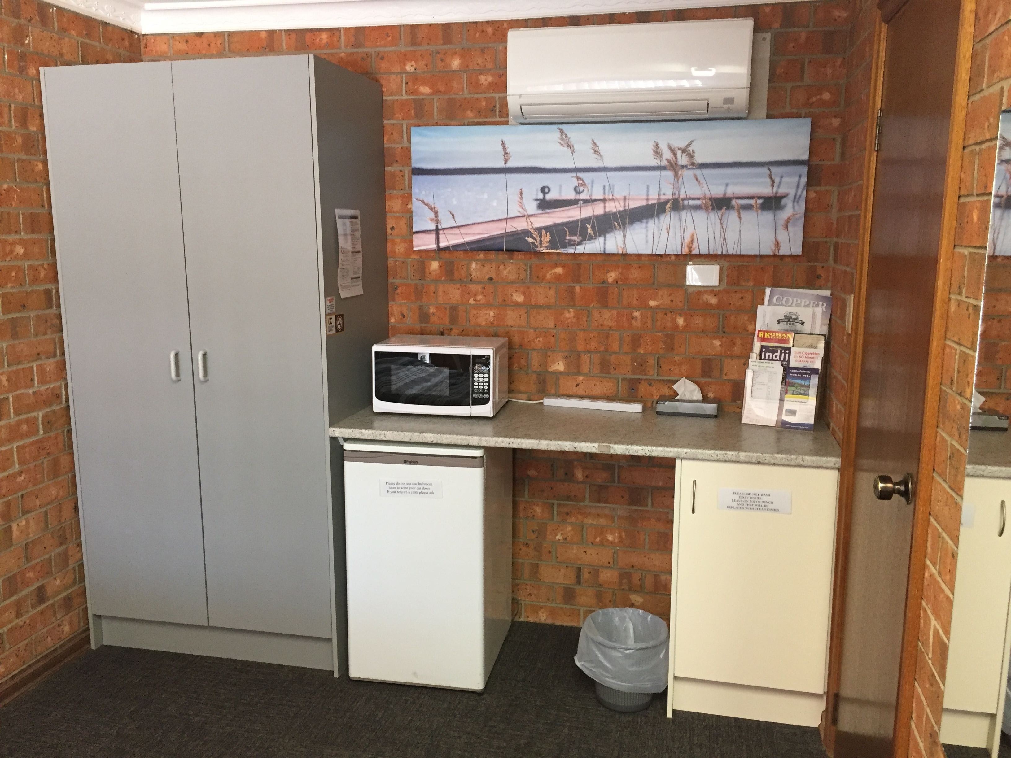 A compact kitchenette with a microwave, a small refrigerator, and a trash bin.
