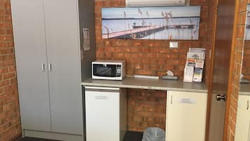 A compact kitchenette with a microwave, a small refrigerator, and a trash bin.