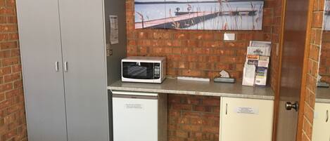 A compact kitchenette with a microwave, a small refrigerator, and a trash bin.