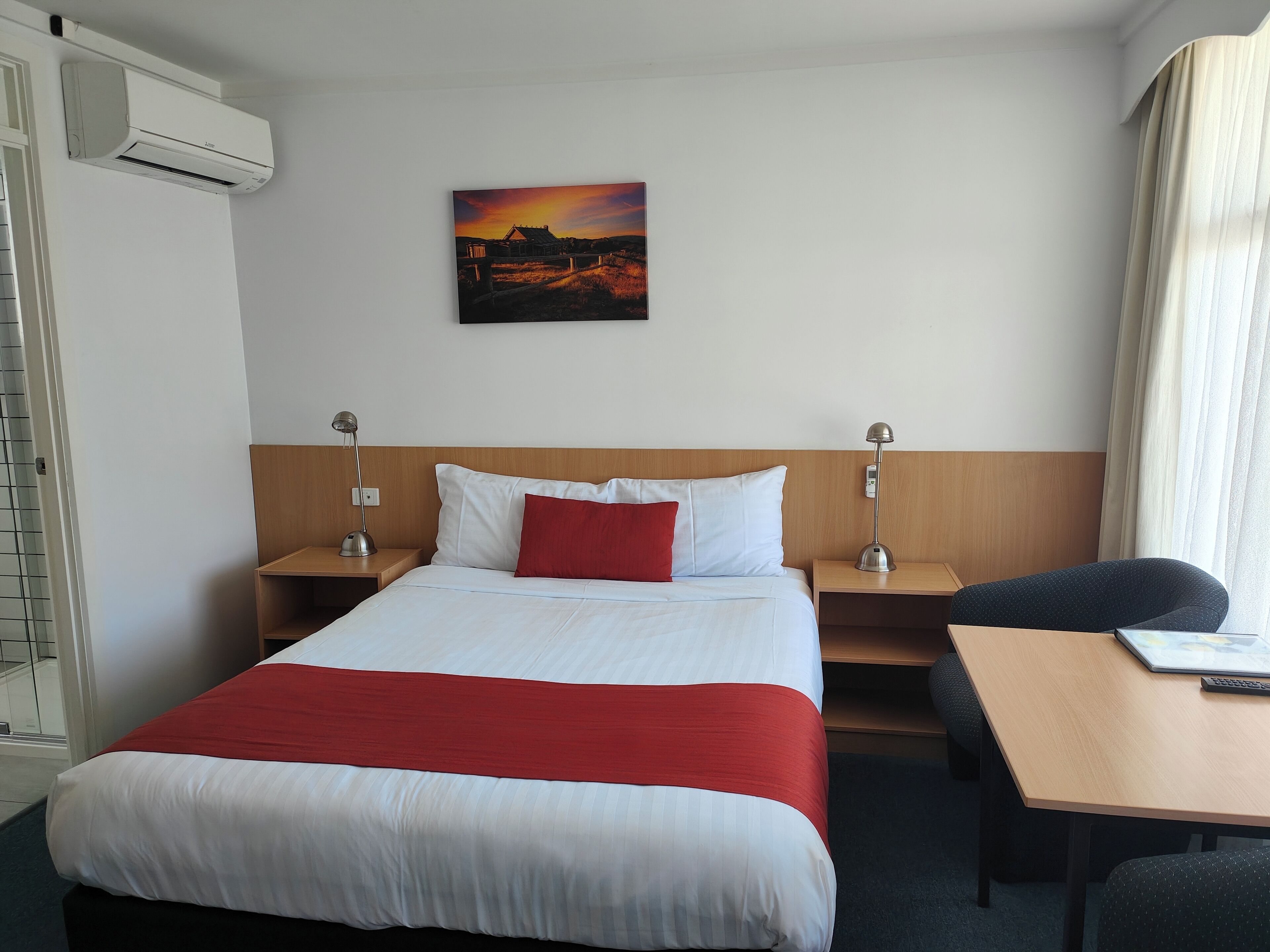 Una habitación de hotel con una cama, dos mesitas de noche, un escritorio y una silla.