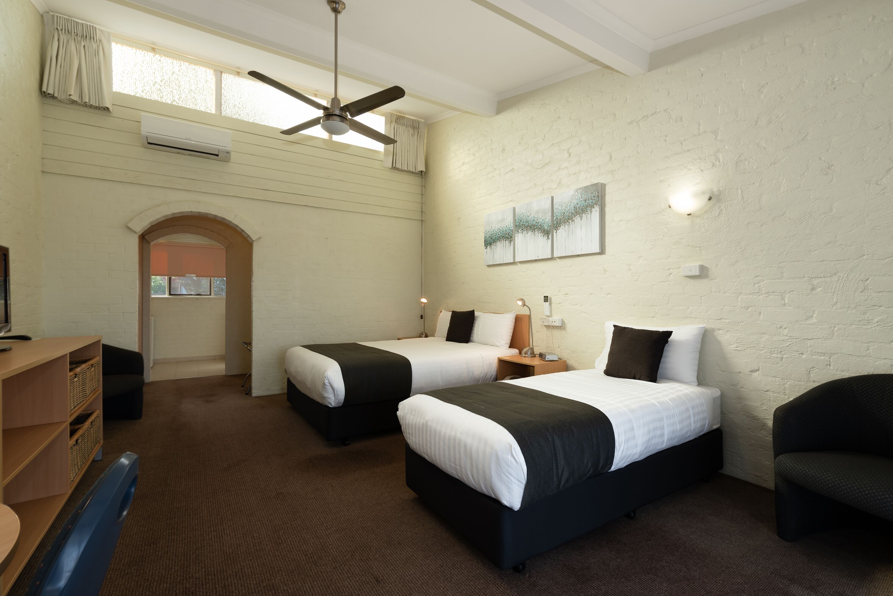 A hotel room with two beds, a desk, a chair, a ceiling fan, and a window with curtains.