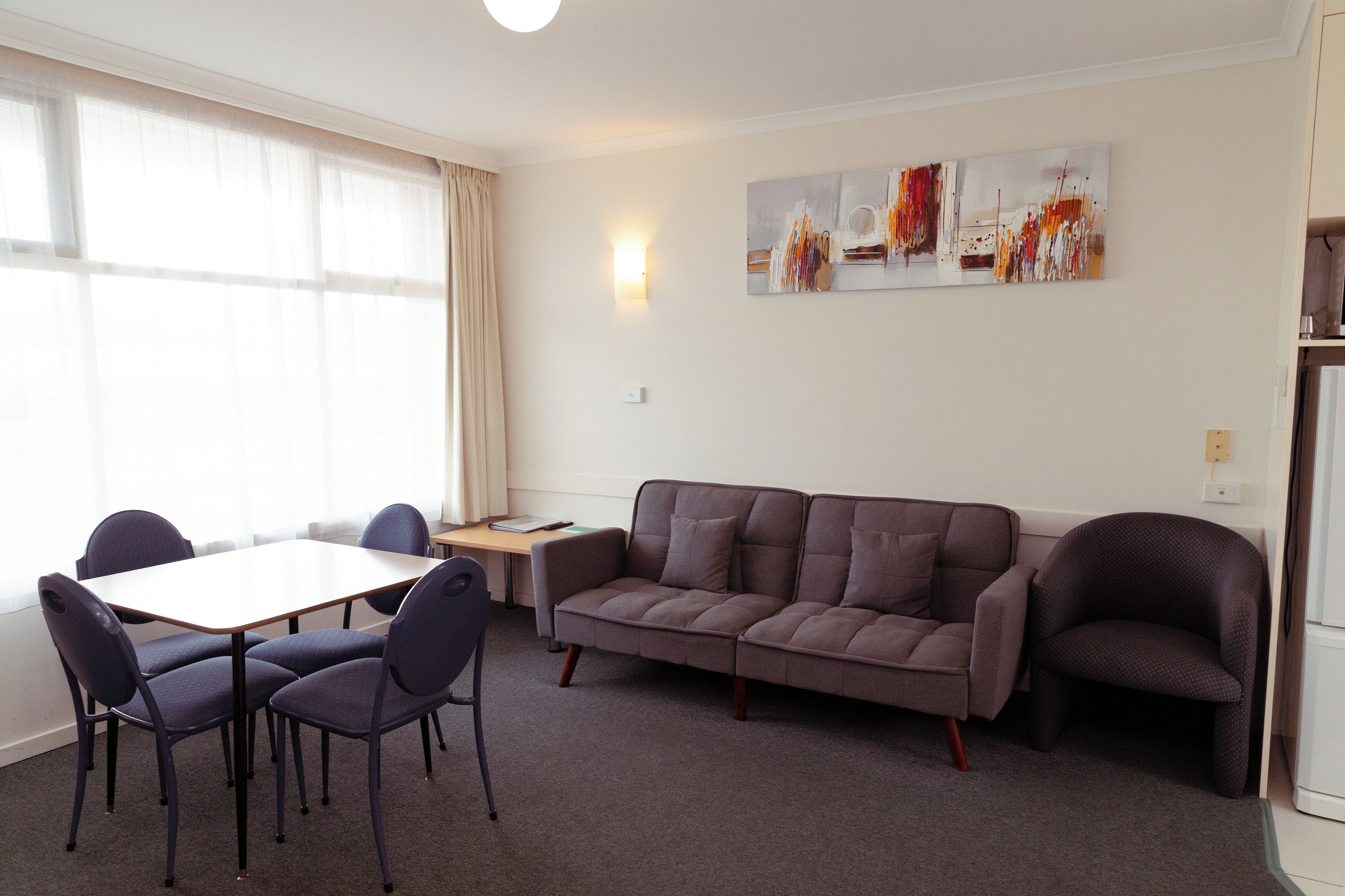 Ein modernes Wohnzimmer mit einer Couch, zwei Sesseln, einem Esstisch mit vier Stühlen und einem kleinen Beistelltisch.