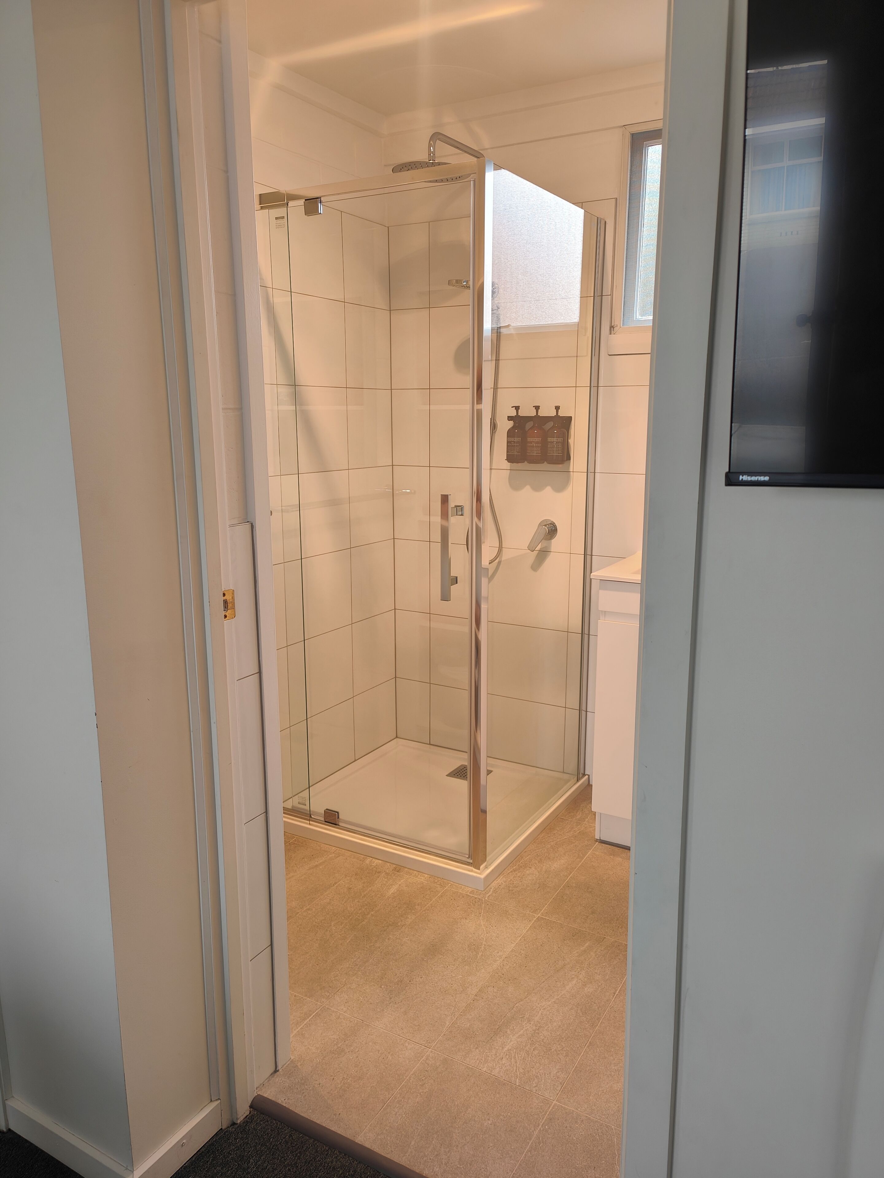 Un baño con ducha acristalada, paredes de azulejos y una puerta blanca.
