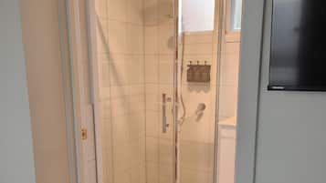 Un baño con ducha acristalada, paredes de azulejos y una puerta blanca.