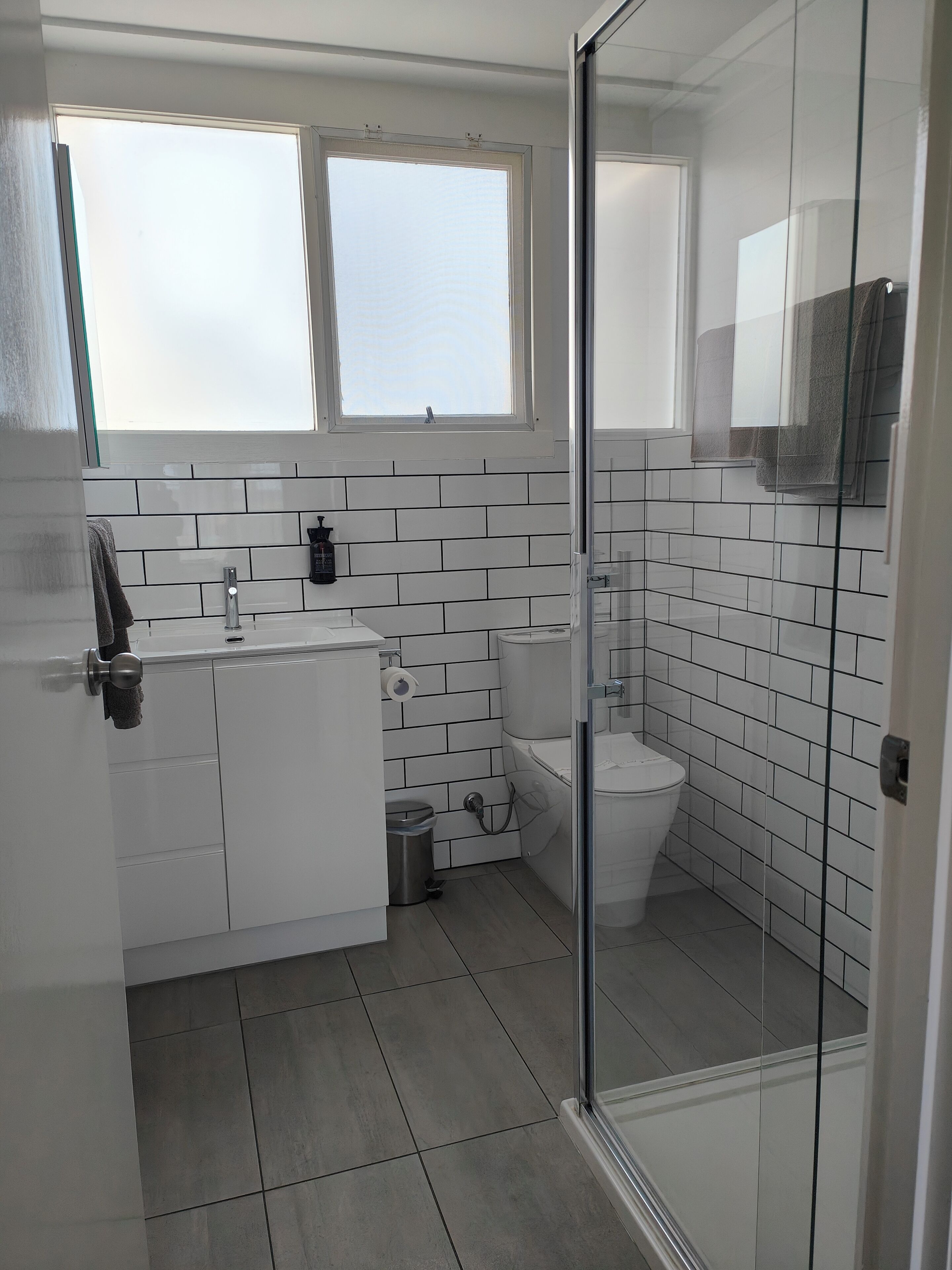 Une salle de bain moderne avec des carreaux blancs, une douche en verre, des toilettes et un lavabo avec un robinet.