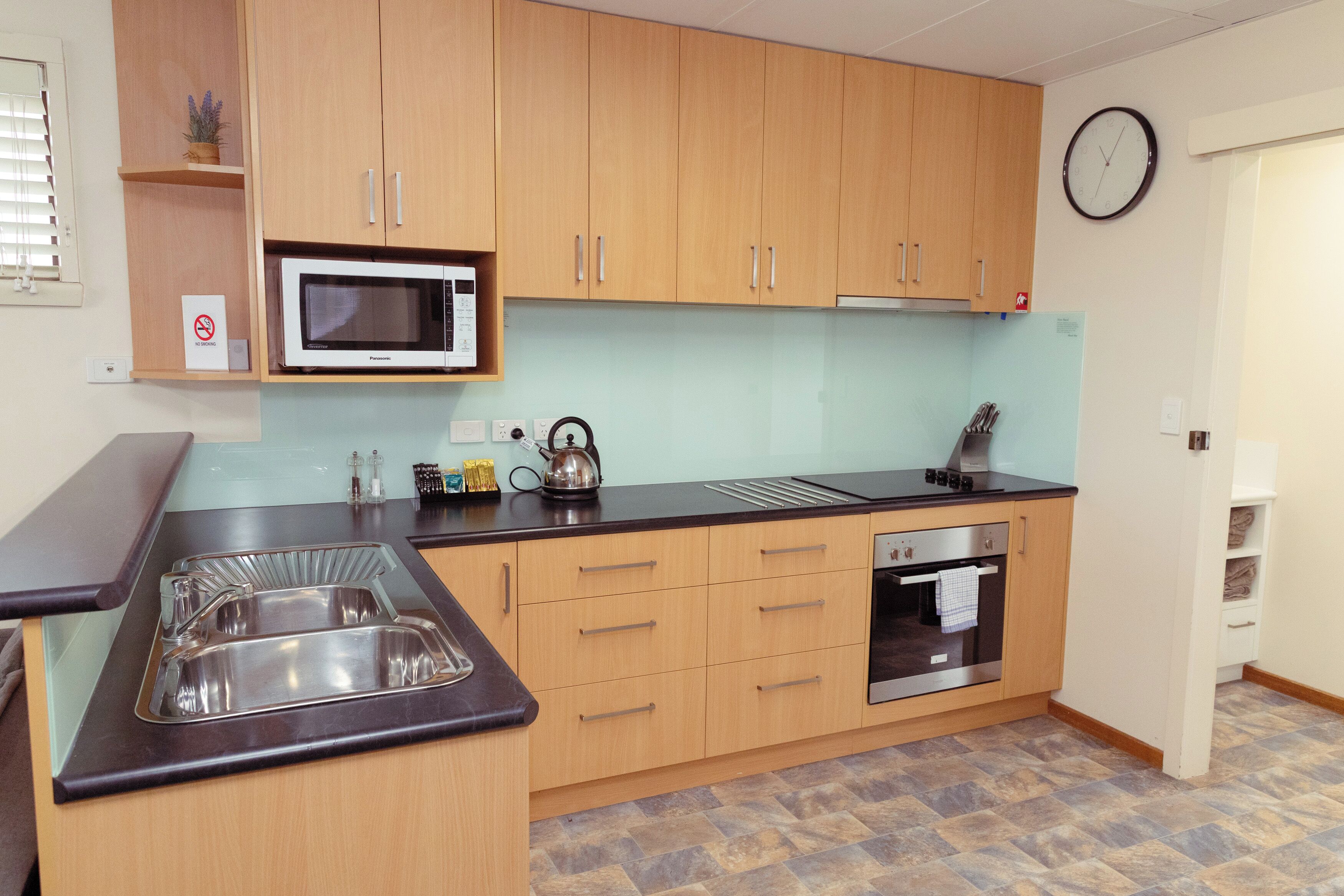 A kitchen with wooden cabinets, a microwave, a kettle, a sink, and an oven.