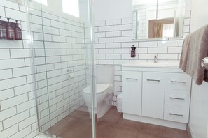 A modern bathroom with white tiled walls, a glass shower enclosure, a white toilet, and a white vanity with drawers.