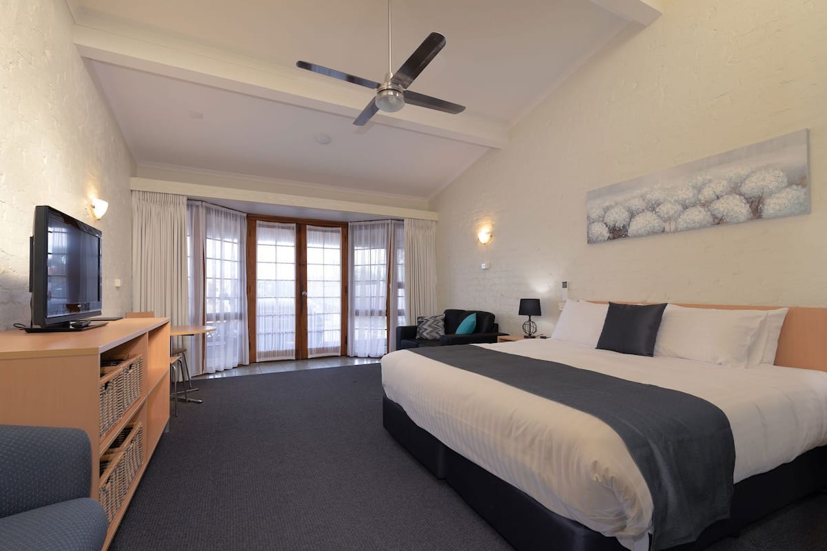 A hotel room with a bed, a TV, a desk, and a ceiling fan.