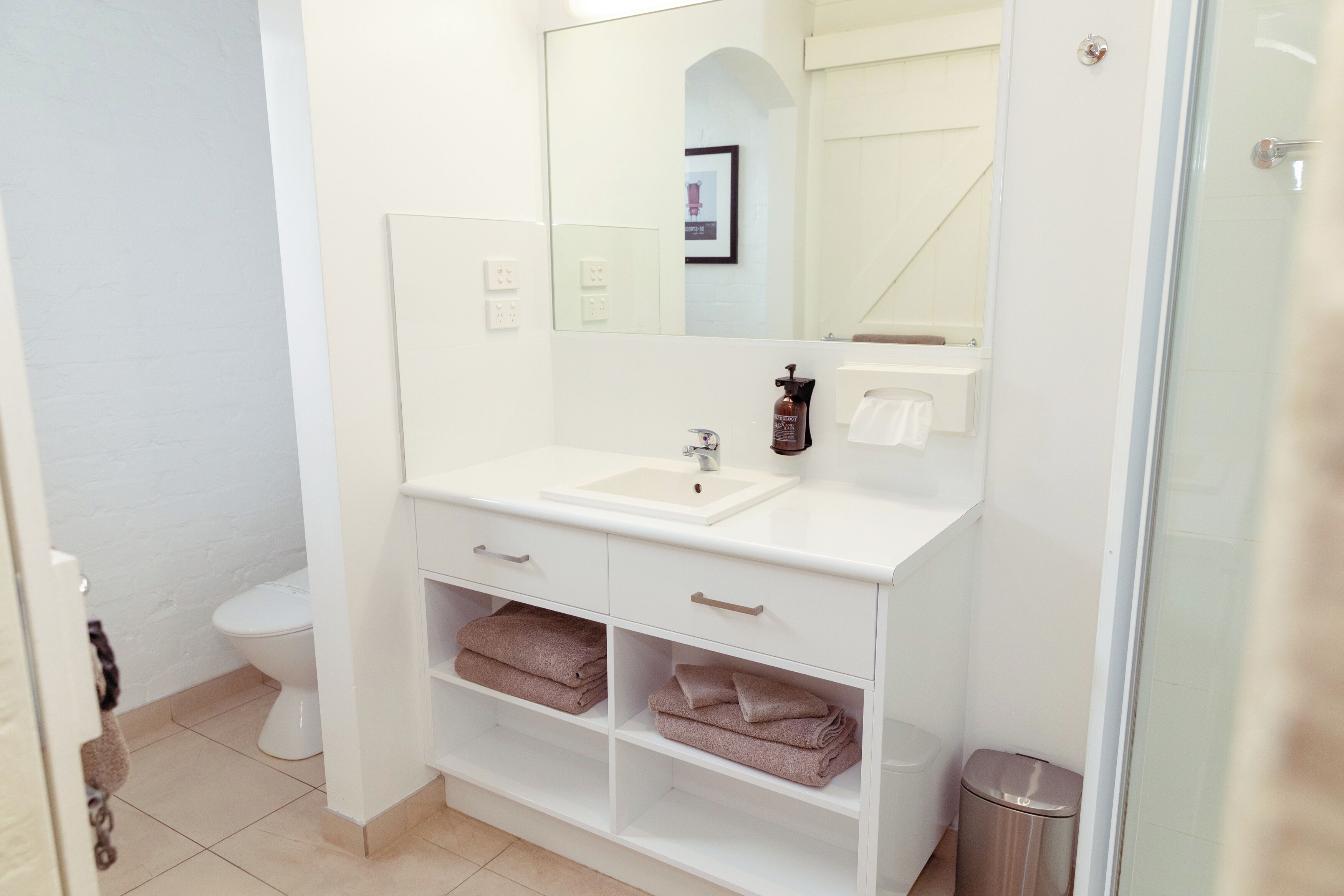 A modern bathroom with a white sink, mirror, and built-in shelves for towels.